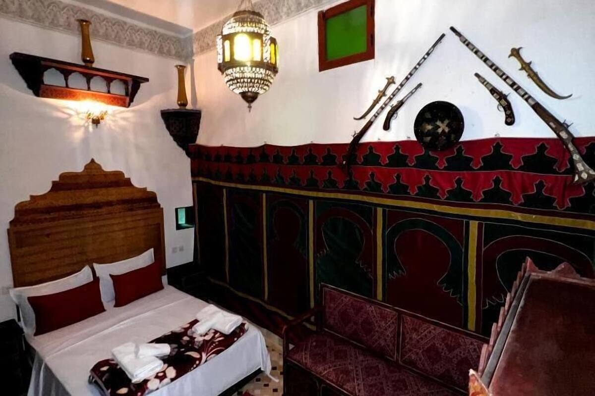 Una habitació amb un llit, una panxa i una paret decorativa amb armes.