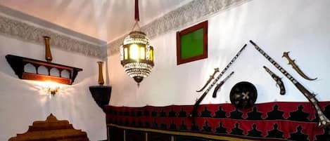 A room with a bed, a bench, and a decorative wall with weapons.