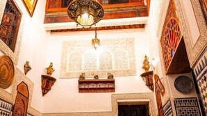 A traditional Moroccan interior with a dining area featuring checkered tile flooring, ornate wooden furniture, and a hanging chandelier. - Riad Dar Kirami  (Fes)