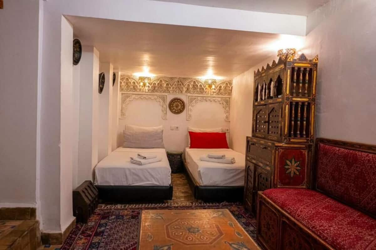 Passadís estret que condueix a una habitació amb dos llits, un sofà vermell i un armari de fusta.