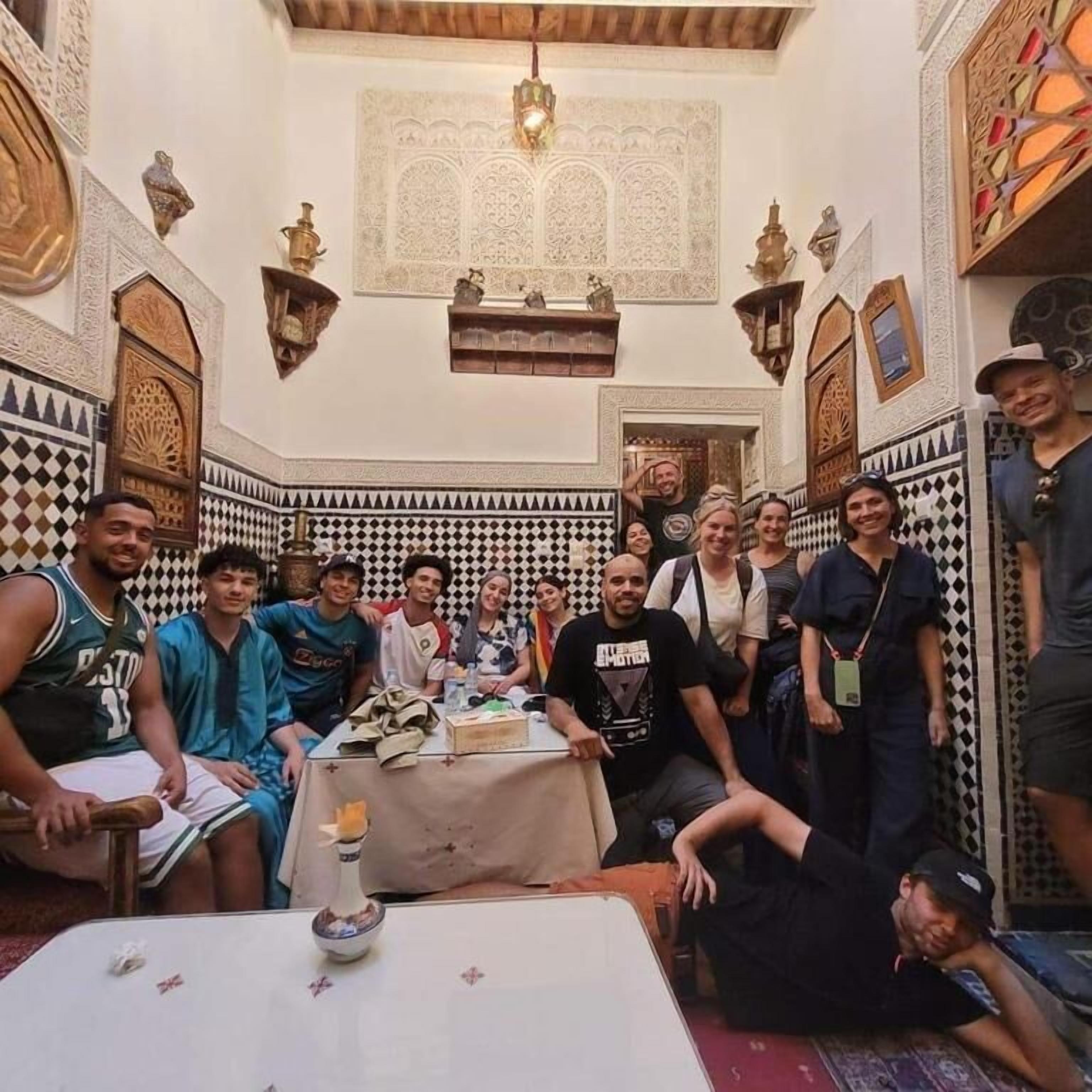 A group of people in a room with intricate tile patterns on the walls and a central table with various items.