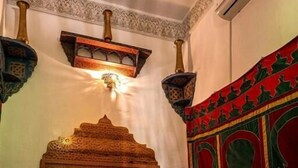 A room with a bed, pillows, a wall-mounted light fixture, and a decorative tapestry. - Riad Dar Kirami  (Fes)