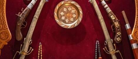 Una exhibición de armas antiguas y platos decorativos sobre un fondo de terciopelo rojo con elaborados grabados de madera.