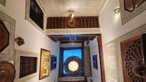 A grand hallway with intricate wooden carvings, a central chandelier, and a large ornate mirror. - Riad Dar Kirami  (Fes)