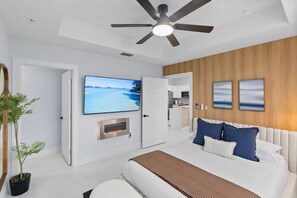 Ein modernes Schlafzimmer mit Bett, Deckenventilator, Fernseher und Kamin.