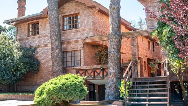 A brick building with a balcony, large trees, and a staircase. - Vacances Centro (Pinamar)