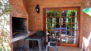 A brick patio with a grill, two plastic chairs, and a wooden table. - Vacances Centro (Pinamar)
