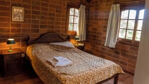 A bedroom with a brick wall, a wooden bed, two bedside tables with lamps, and a window with curtains. - Vacances Centro (Pinamar)