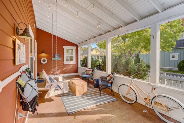 A covered porch with a swing, wicker chairs, a bicycle, and a view of the neighborhood.