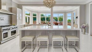 Une cuisine moderne dotée d’un grand îlot central, d’appareils électroménagers en acier inoxydable et d’un lustre.