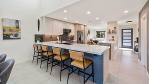 Uma cozinha moderna com uma ilha central, banquetas e iluminação embutida.