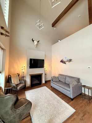 A spacious living room with a fireplace, a sofa, a chair, and a TV mounted on the wall. - Peaceful 2-bedroom house in charming Seeley Lake (Seeley Lake)
