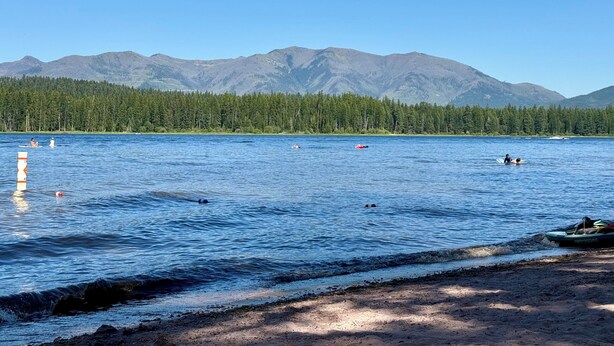 A lake with mountains in the background, a sandy beach, and a jet ski. - Peaceful 2-bedroom house in charming Seeley Lake (Seeley Lake)