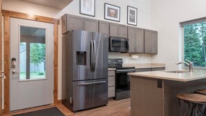 A modern kitchen with stainless steel appliances, wooden cabinets, and a large island with bar stools. - Peaceful 2-bedroom house in charming Seeley Lake (Seeley Lake)