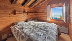 Un dormitorio de cabaña de madera con una cama, una ventana con vista a la montaña y un estante pequeño.