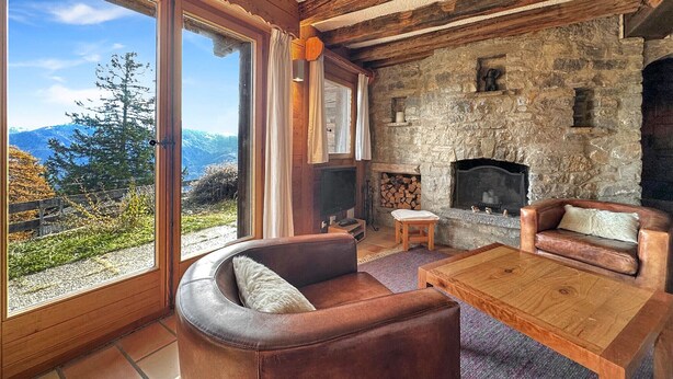 Una sala de estar acogedora con chimenea de piedra, sofás de cuero y ventanas amplias con vistas a la montaña.