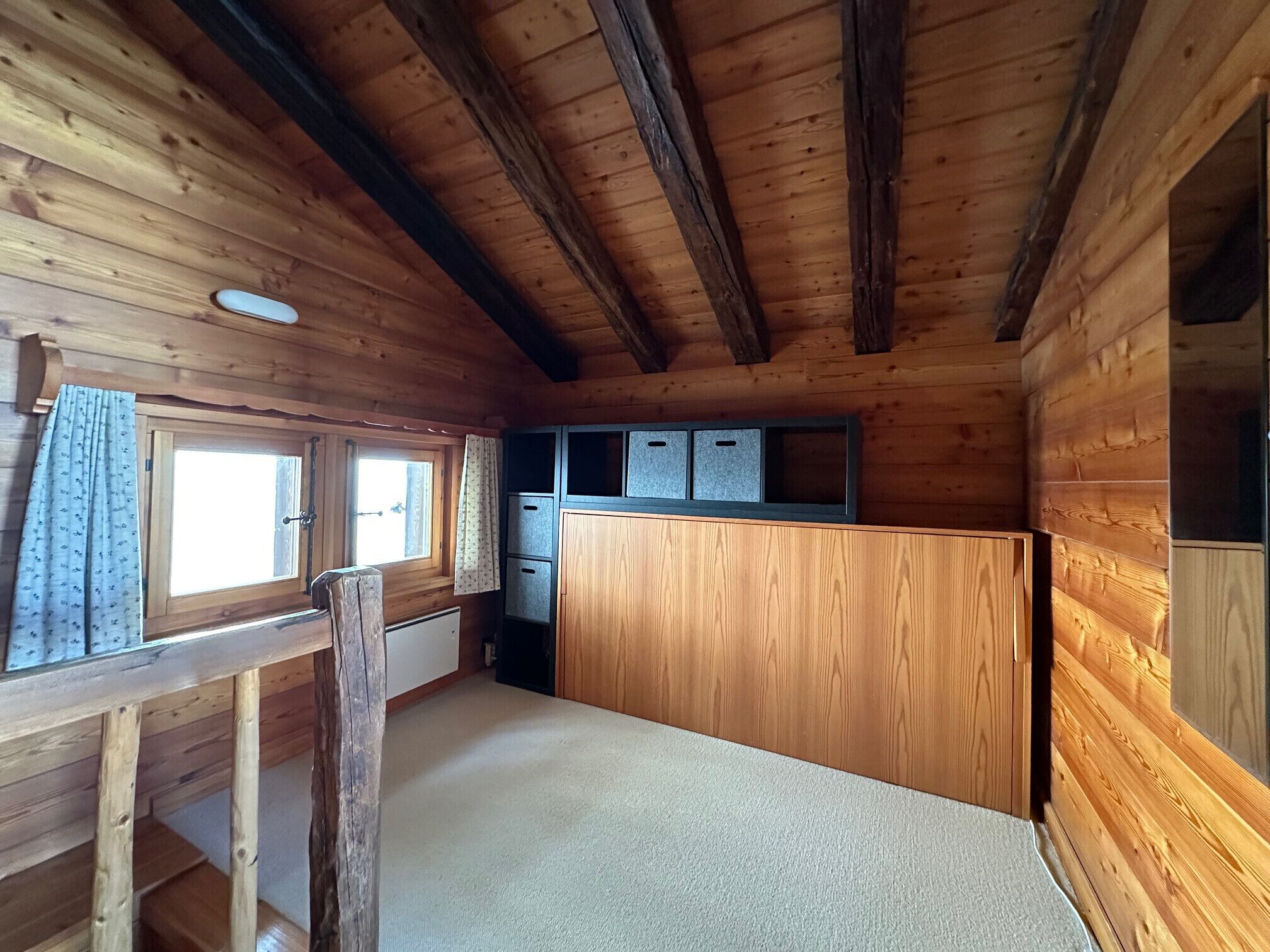 A wooden cabin interior with a kitchen area, a window with a curtain, and a wooden bench.