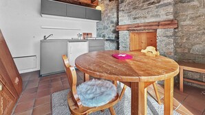 Une cuisine chaleureuse avec un mur en pierre, des poutres en bois et une table ronde en bois, accompagnée d’une chaise.