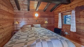 Une chambre confortable dans un chalet en bois, avec une couverture à carreaux sur le lit, deux lampes de chevet, une fenêtre donnant sur un beau paysage et un luminaire au plafond.