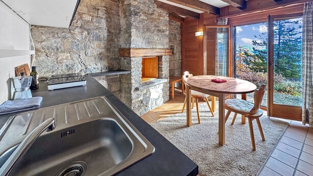 Une cuisine rustique avec un mur en pierre, des poutres en bois, un évier et un coin repas comprenant une table et des chaises.