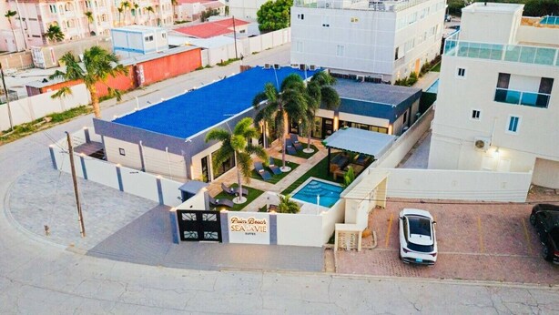 Ett hotell med en swimmingpool, palmer och en skylt med texten ”Palm Beach Sea Lavie Suites”.