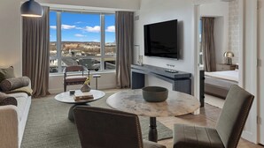 A modern hotel room with a large window, a flat-screen TV, a round dining table, and a comfortable seating area. - Lux 2BR in Assembly Square | Pool & Fitness Center (Somerville)