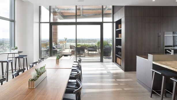 A modern kitchen with a large island, dark wood cabinetry, and a view of the city through large windows. - Lux 2BR in Assembly Square | Pool & Fitness Center (Somerville)