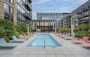 A rooftop swimming pool with lounge chairs and a covered seating area, surrounded by modern buildings. - Stylish 1BR in Assembly Square | Pool, Gym & Views (Somerville)