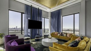 A modern living room with a large TV, yellow sofas, purple chairs, and a city view. - Stylish 1BR in Assembly Square | Pool, Gym & Views (Somerville)