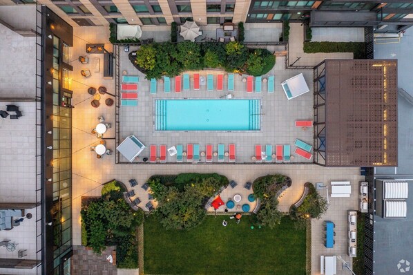 An aerial view of a rooftop pool area with multiple lounge chairs and a central swimming pool. - Stylish 1BR in Assembly Square | Pool, Gym & Views (Somerville)