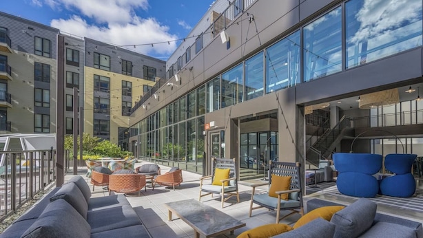 A modern outdoor seating area with sofas and chairs, a staircase, and a glass building facade. - Stylish 1BR in Assembly Square | Pool, Gym & Views (Somerville)