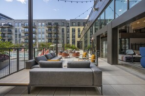 A modern outdoor seating area with grey sofas and chairs, a small table, and a view of the building's exterior. - Stylish 1BR in Assembly Square | Pool, Gym & Views (Somerville)