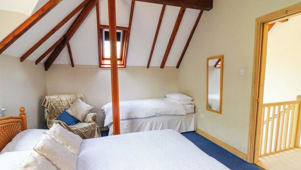 A bedroom with two beds, a wooden ceiling, a window, and a mirror. - Gaer Hall (Welshpool)