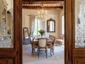 Ein Esszimmer mit einem Holztisch, gedeckt für vier Personen, umgeben von Stühlen. Eine Chandelier hängt von der Decke, und ein Spiegel befindet sich an der Wand.