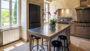 A modern kitchen with a central island, stainless steel appliances, and a view of greenery outside. - Bastide of the Rose Comtesse – The Art of Intimate Luxury in Provence (Ventabren)