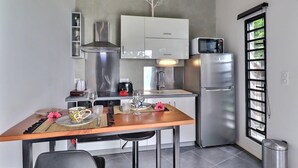 A compact kitchen with a dining table, stainless steel appliances, and a window with a view. - Moorea Horizon – Stunning Panoramic View – Pool (Papeete)