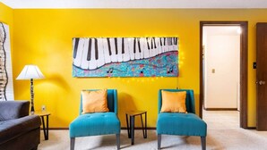 A room with two teal armchairs, a yellow wall, and a large abstract painting.