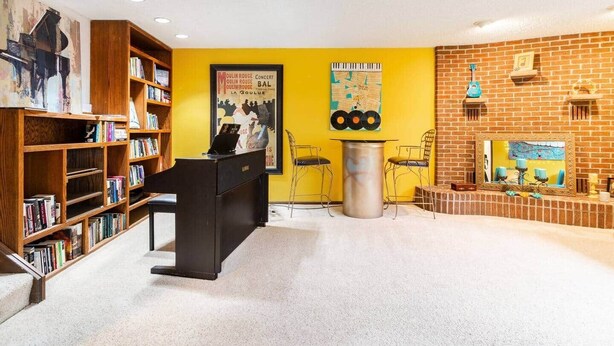 A library with bookshelves, a piano, a poster, and a brick fireplace.