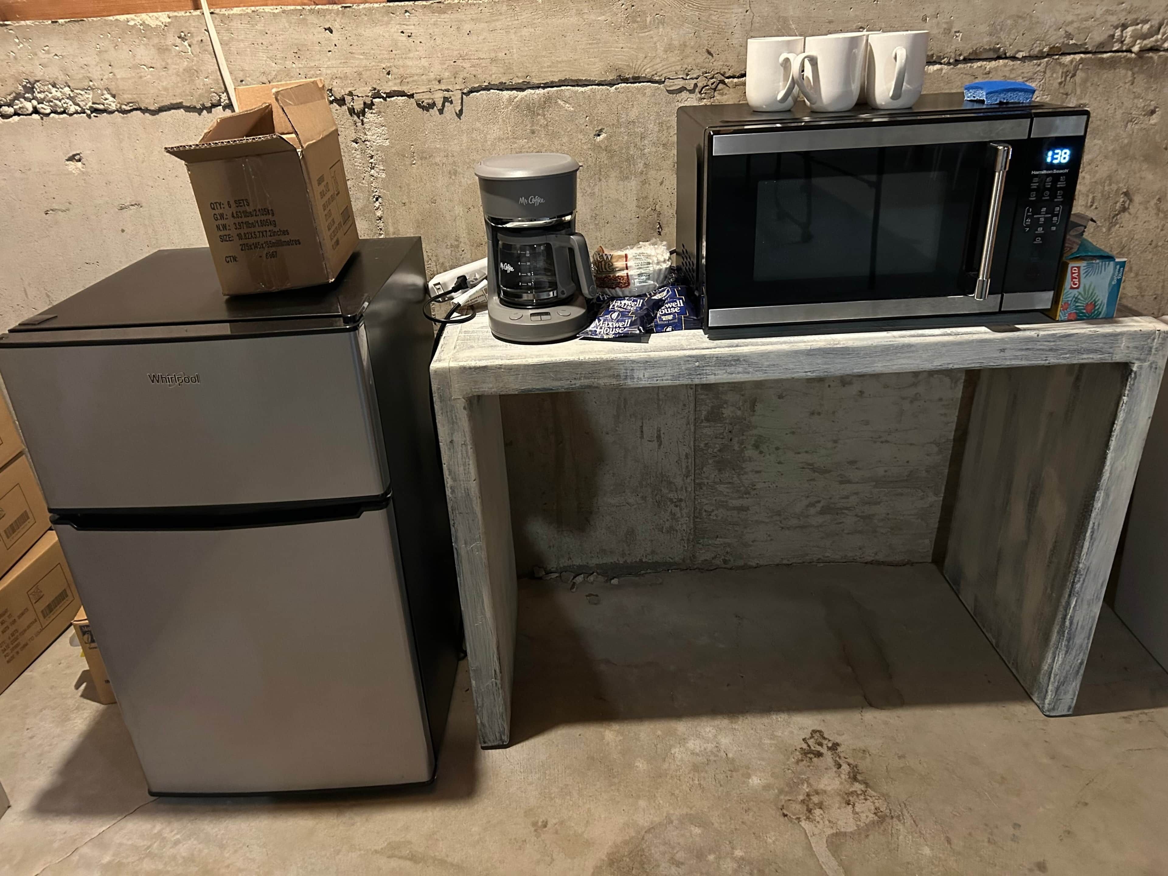 A compact kitchenette with a refrigerator, coffee maker, and microwave on a concrete countertop.