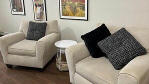Een zithoek met twee beige fauteuils, waarvan één een zwart kussen en de andere een kussen met zwart-wit patroon heeft. Daartussen staat een klein, wit bijzettafeltje.