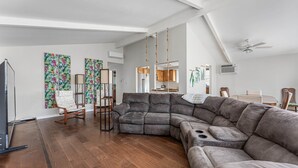 Een ruime woonkamer met een grote hoekbank, houten vloeren en een plafondventilator.