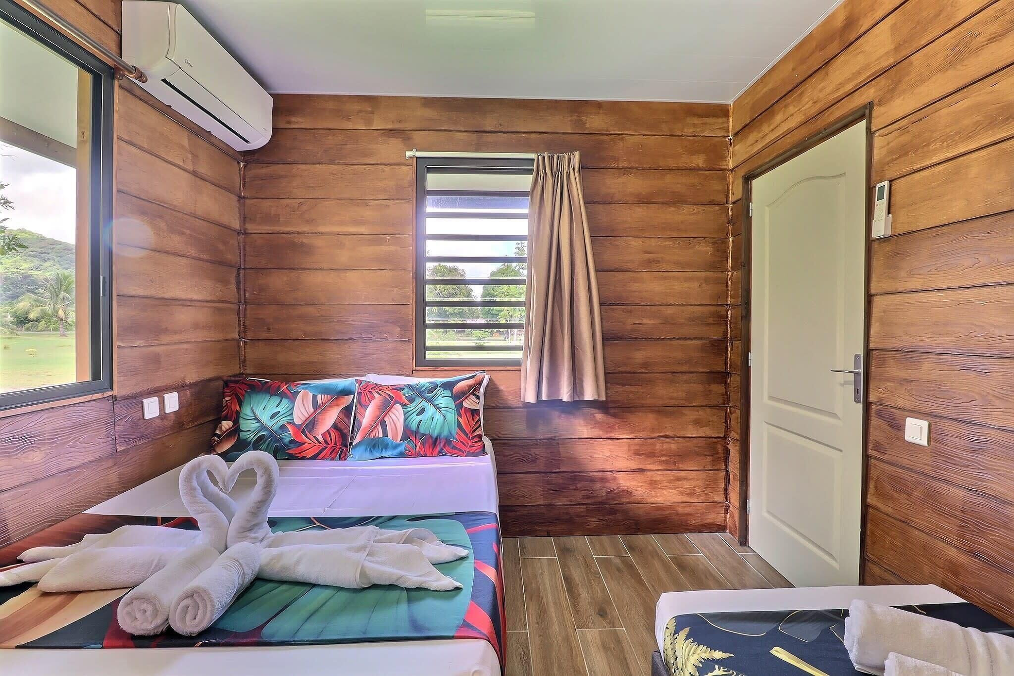 A wooden-paneled room with a bed, a window with curtains, and an air conditioning unit.