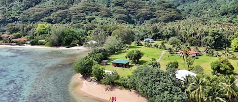 A coastal property with a beach, lush greenery, and several buildings with green roofs.
