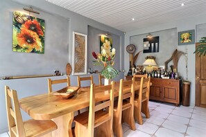 Ein Essbereich mit einem Holztisch und Stühlen, einer Vase mit Blumen und einem Schrank mit Flaschen.