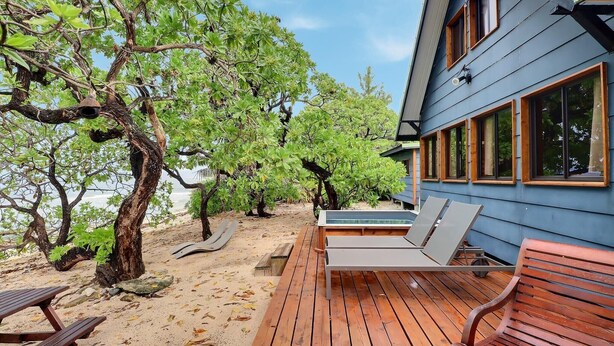 Una terraza de madera con sillones de descanso, piscina y un edificio con ventanales grandes.