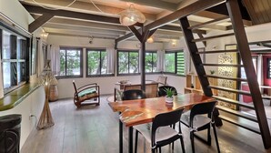 Un comedor amplio con una mesa y sillas de madera, ventanas grandes con cortinas y una lámpara colgante.