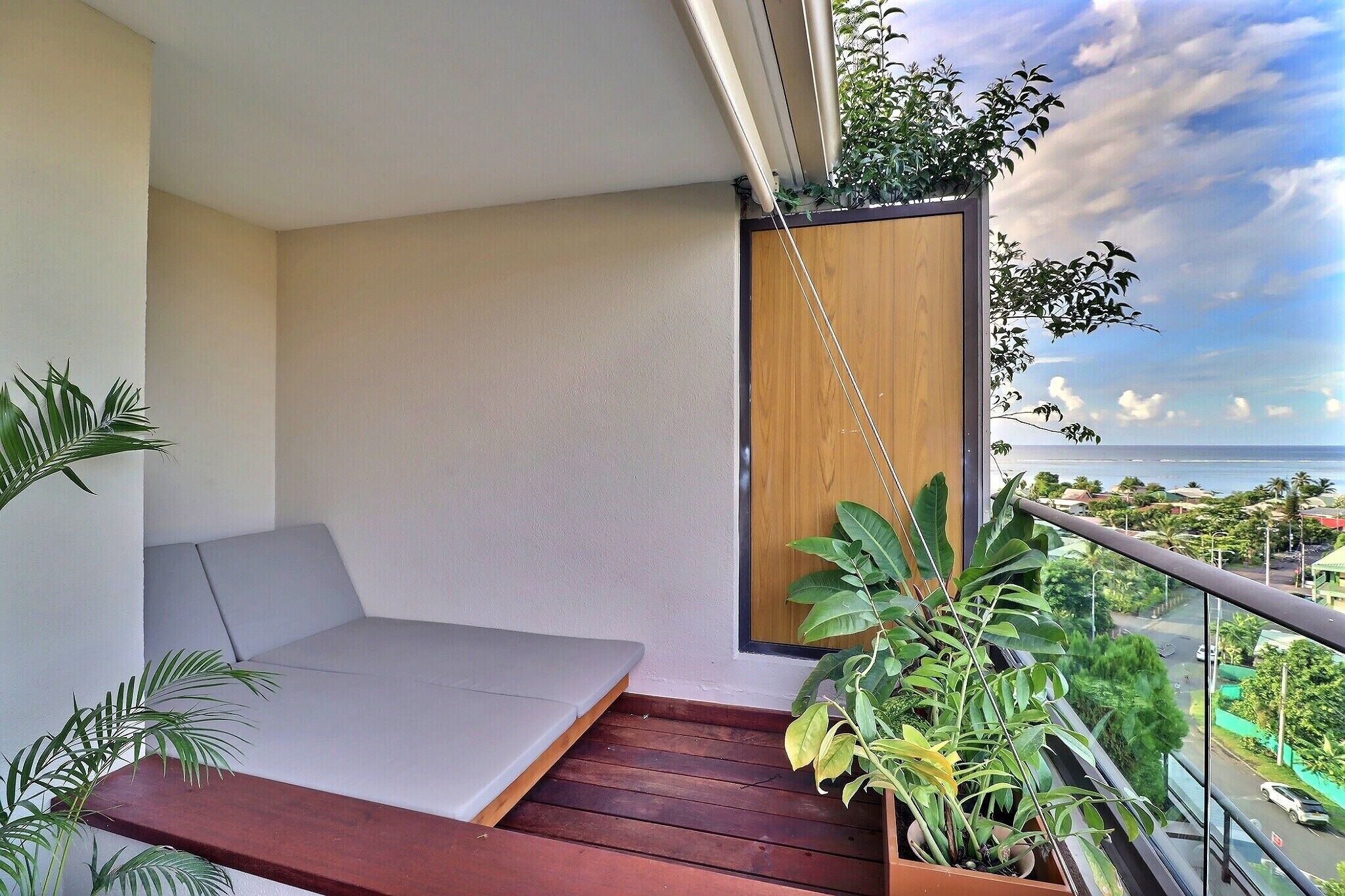 Een balkon met houten vloer, een zithoek met kussens en potplanten.
