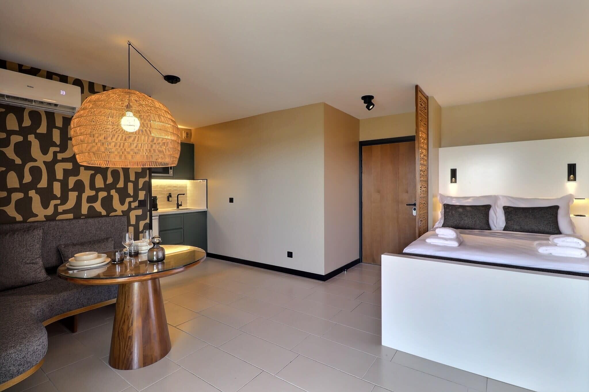 Una habitación de hotel moderna con sofá, una mesa redonda de madera, una cama con almohadas y una lámpara colgante.