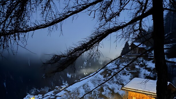 Une cabane en bois avec un toit enneigé, une terrasse en bois et un escalier menant à l’entrée.