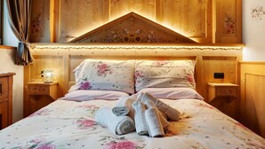 Une chambre à coucher en bois avec un papier peint à motifs floraux, un lit avec une literie à motifs floraux et une table de chevet avec une lampe.